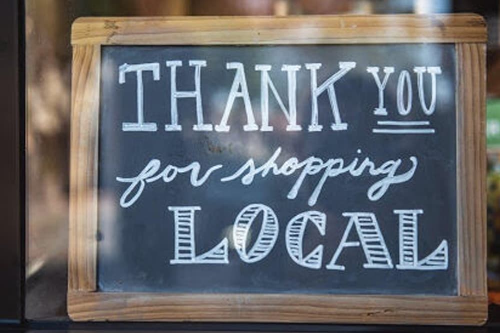 A chalkboard sign with a friendly message: "Thank you for shopping local," framed in rustic wood, encouraging community support for local businesses.